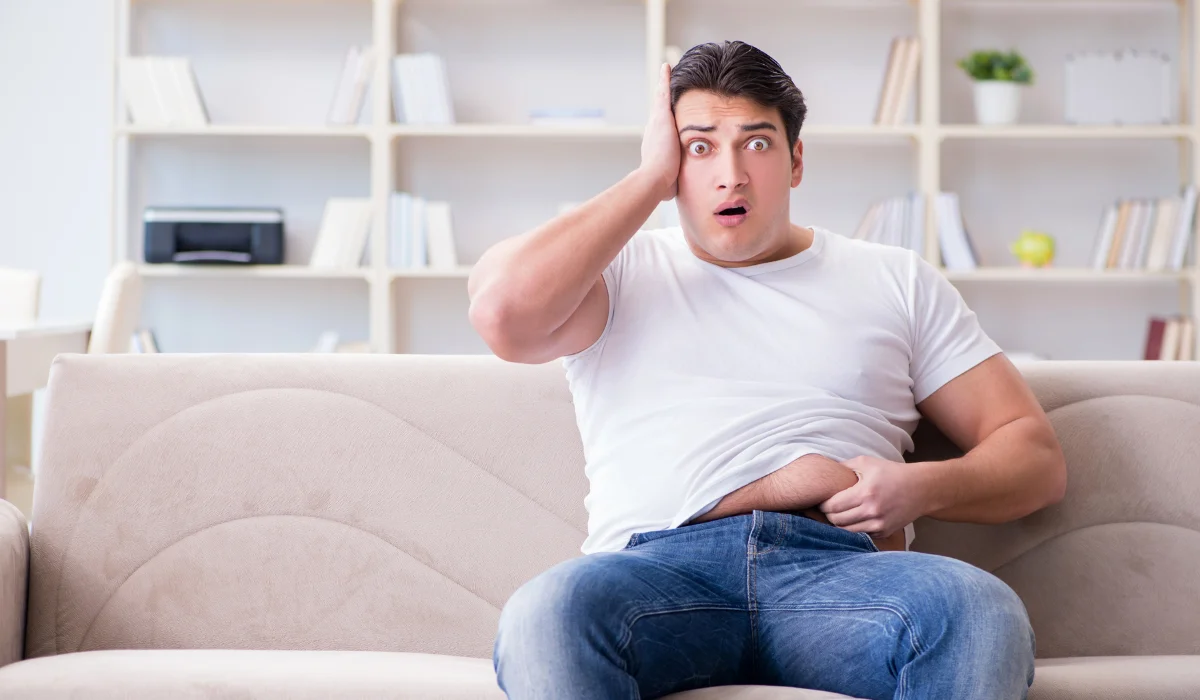 Man sitting down while holding his belly fat.